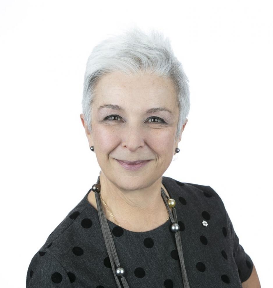 Dr. Catherine Zahn profile picture shows her smiling with a closed mouth. She has a silver haired pixie cut and is wearing a dark grey top with black polka dots, grey pearl earrings and a statement necklace